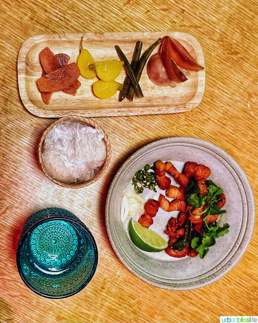 plate of pickled food with plate of pork belly on a wood table.