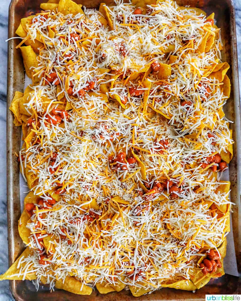 adding Tex-Mex cheese to pinto beans and tortilla chips for sheet pan nachos