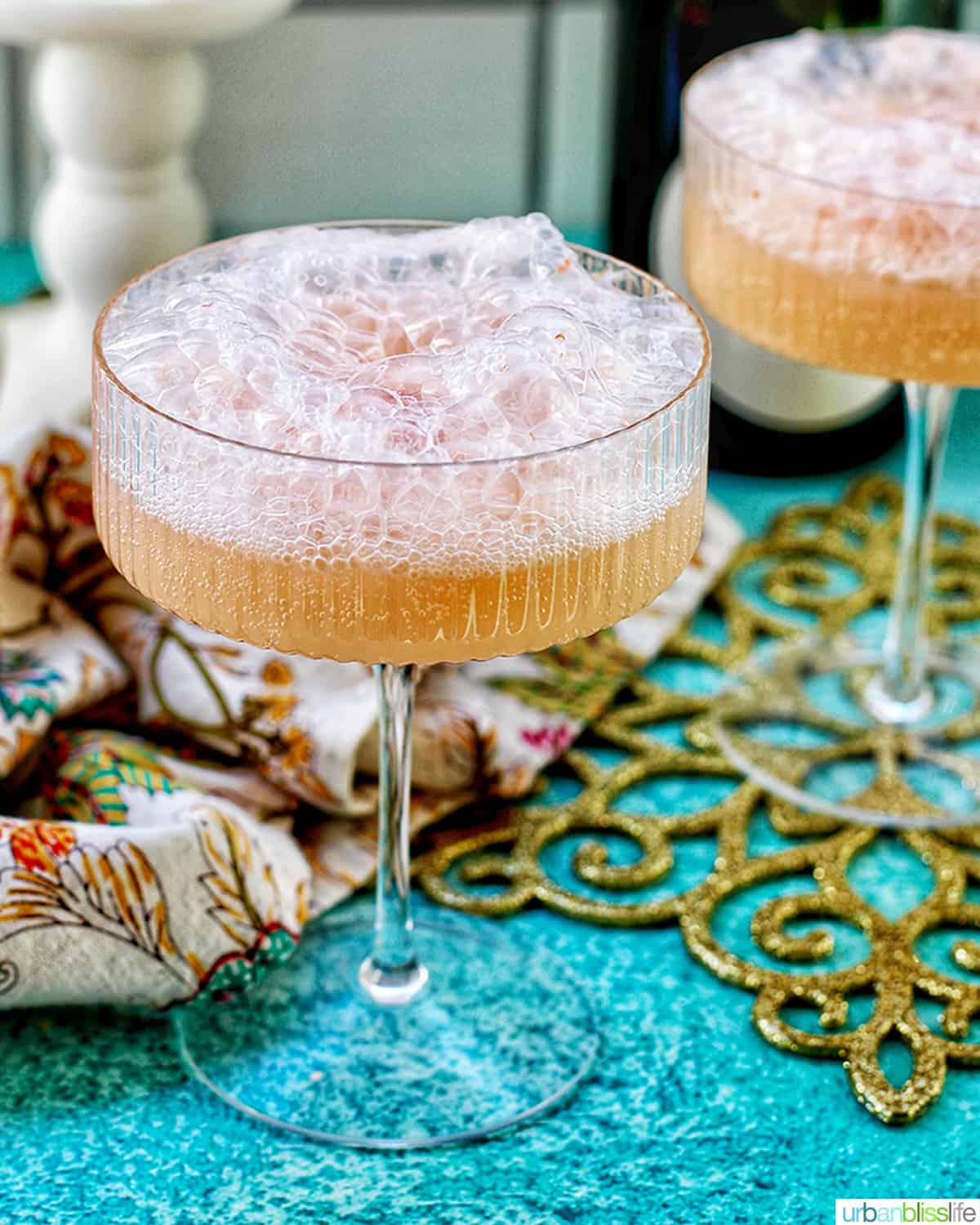two glasses of champagne sherbet floats with twinkling lights and Champagne bottle in background and colorful decor.