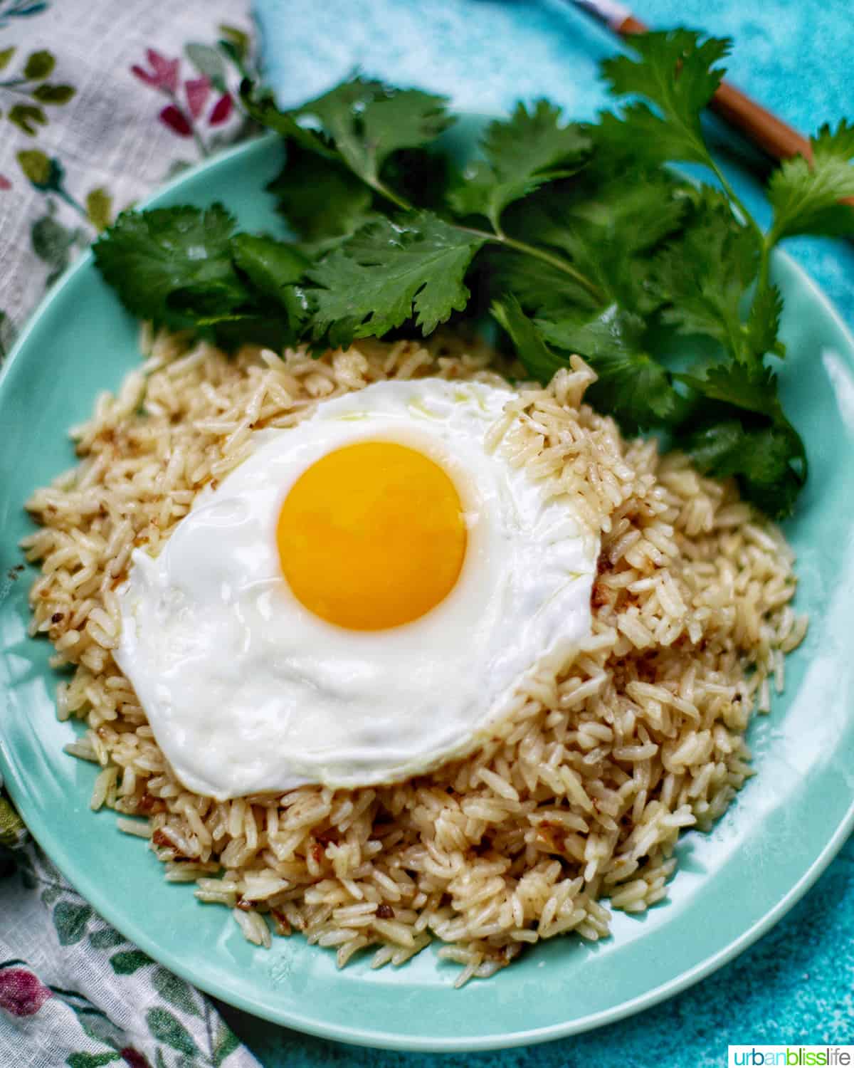 instant pot garlic rice with a side of green herbs on green plate and colorful napkin topped with fried egg.