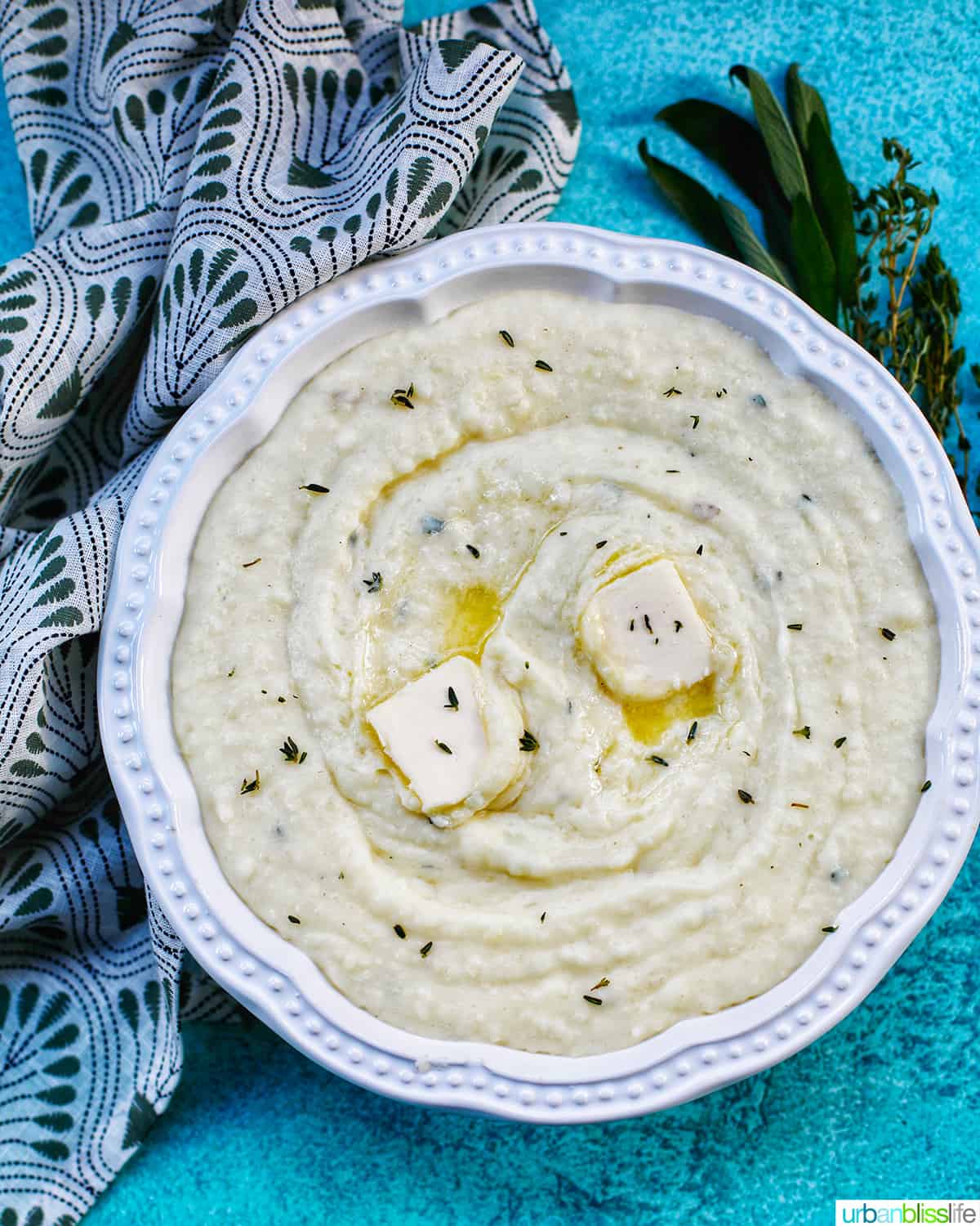 Instant Pot Garlic Mashed Potatoes in a bowl with pats of melting butter and herbs.