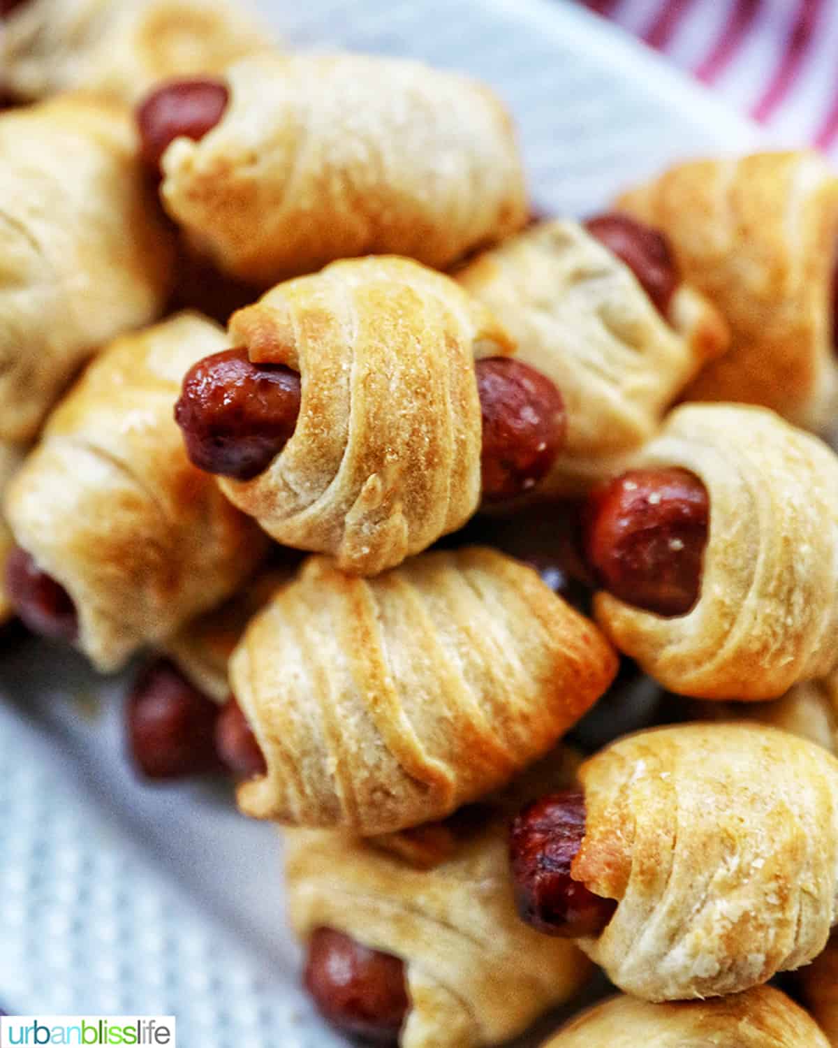 dozens of Air Fryer Pigs in a Blanket stacked on top of a white plate.