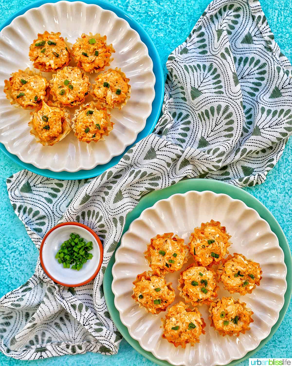 several buffalo chicken bites on two plates with a green and white napkin and small bowl of chopped green onions.