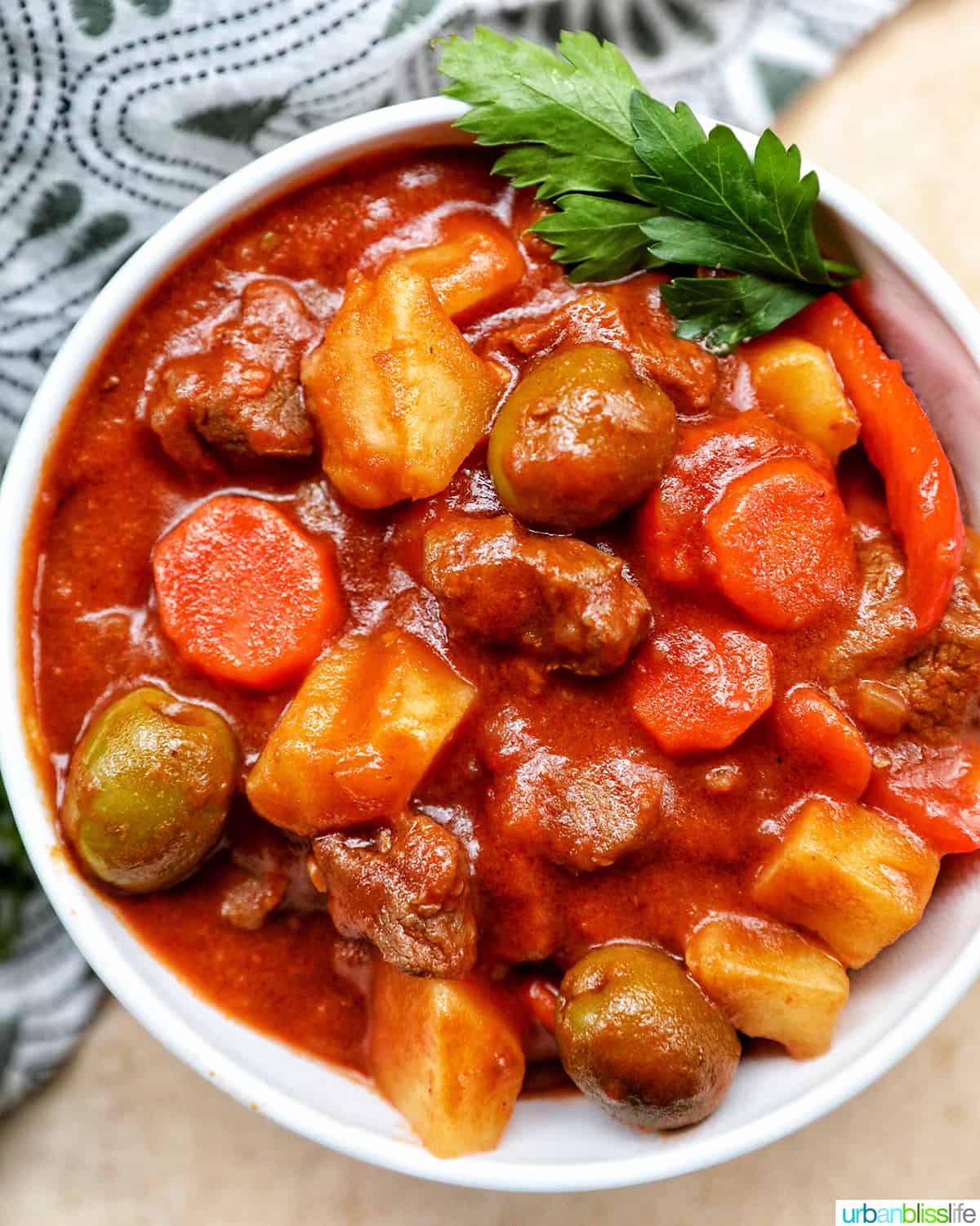 closeup bowl of Filipino beef caldereta stew with potatoes, carrots, olives in a white bowl and parsley.