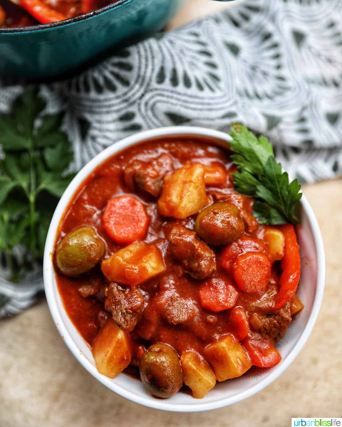 single bowl of Filipino beef caldereta stew with potatoes, carrots, red peppers, green olives on a green and white napkin.
