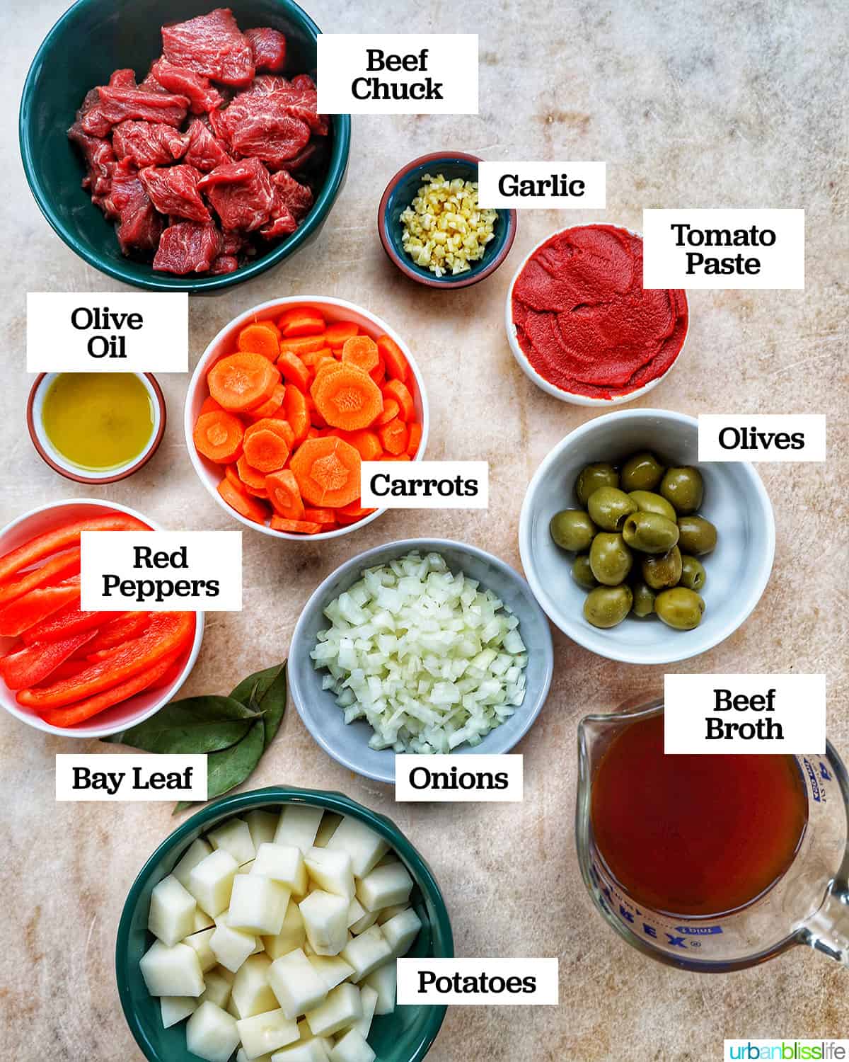 bowls of ingredients like steak, carrots, potatoes, and red bell peppers, to make beef caldereta on a yellow faded table.