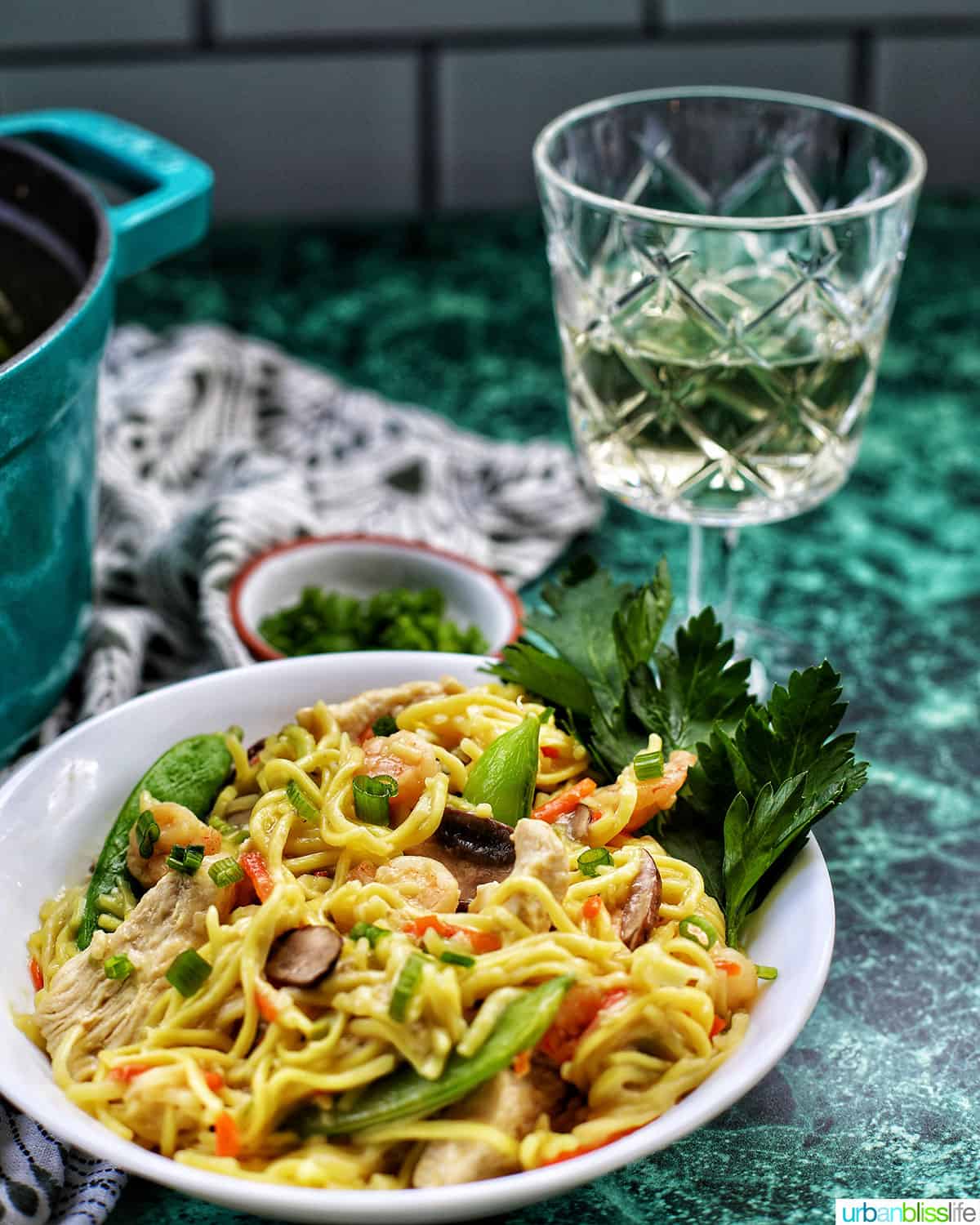 white wine with bowl of adding shrimp to Filipino pancit canton noodles with shrimp, chicken, and vegetables.