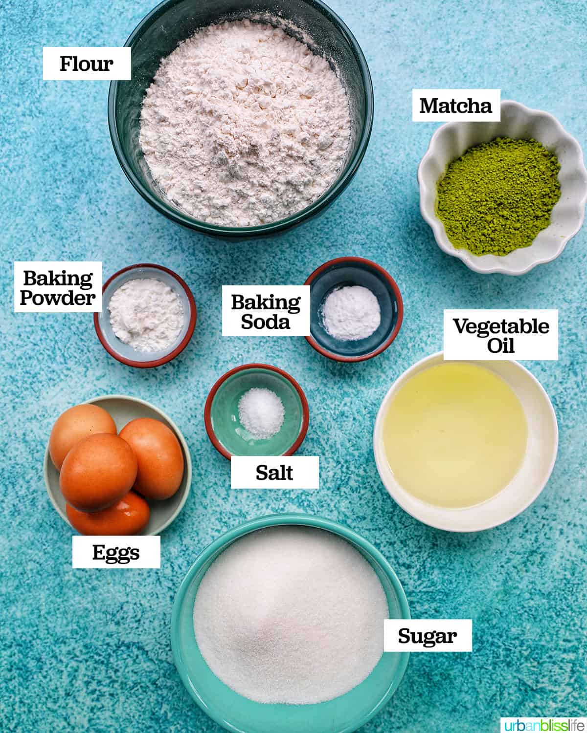 bowls of ingredients to make matcha crinkle cookies on a bright blue background.
