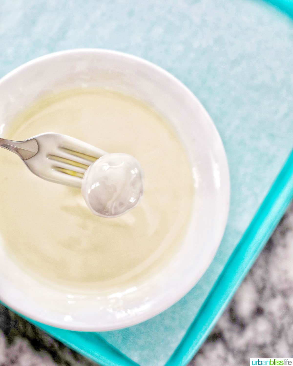 fork dipping cookie dough truffle into melted white chocolate