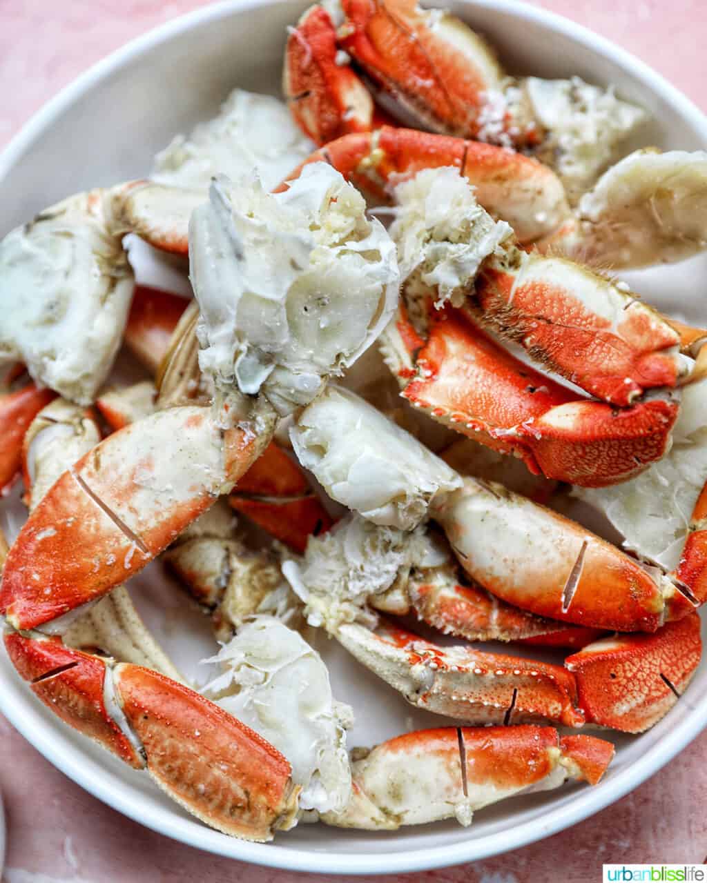 crab legs cracked and laying in a white bowl on a peach table.