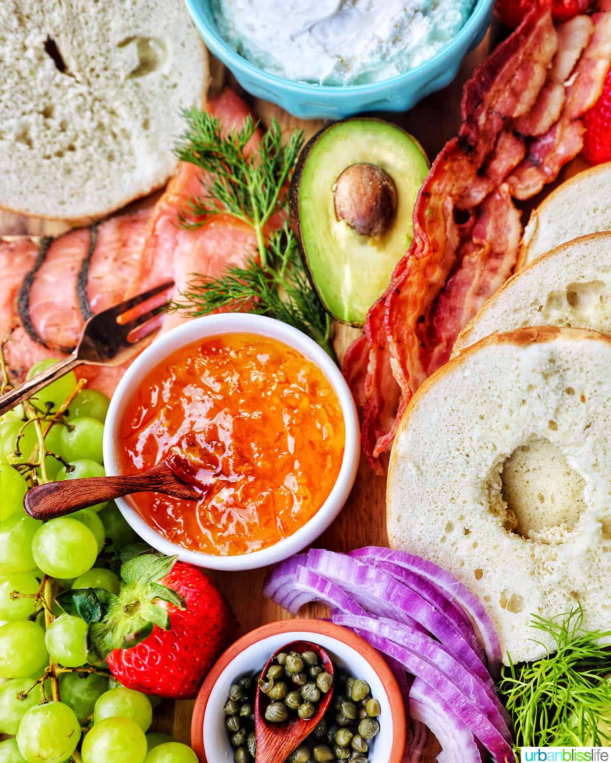 orange marmalade surrounded by fruit,veggies, bagels, bacon