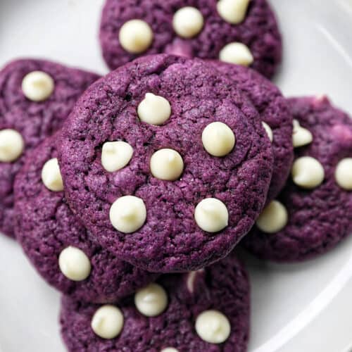 ube white chocolate chip cookies stacked on top of one another on a white plate.