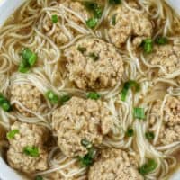 soup of meatballs and thin noodles in a white bowl.