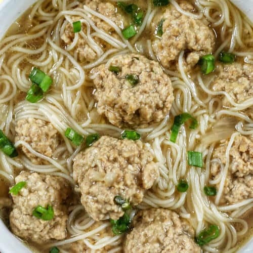 soup of meatballs and thin noodles in a white bowl.