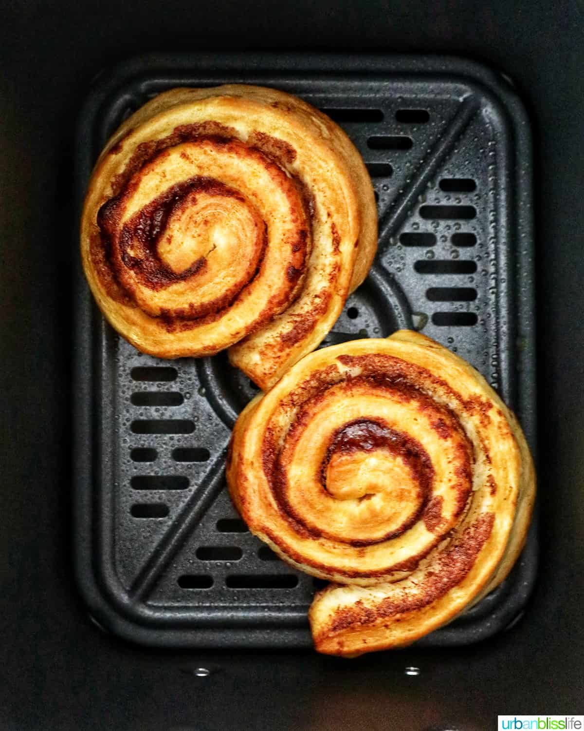 two air fried cinnamon rolls in the air fryer basket
