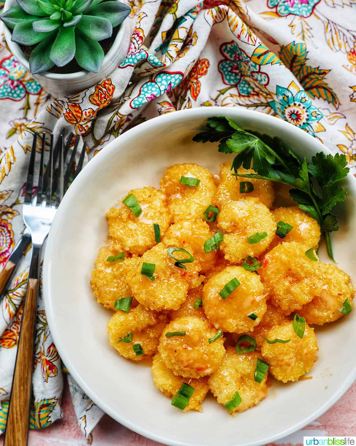 air fryer bang bang shrimp garnished with green onions in a white bowl with forks and a colorful napkin.