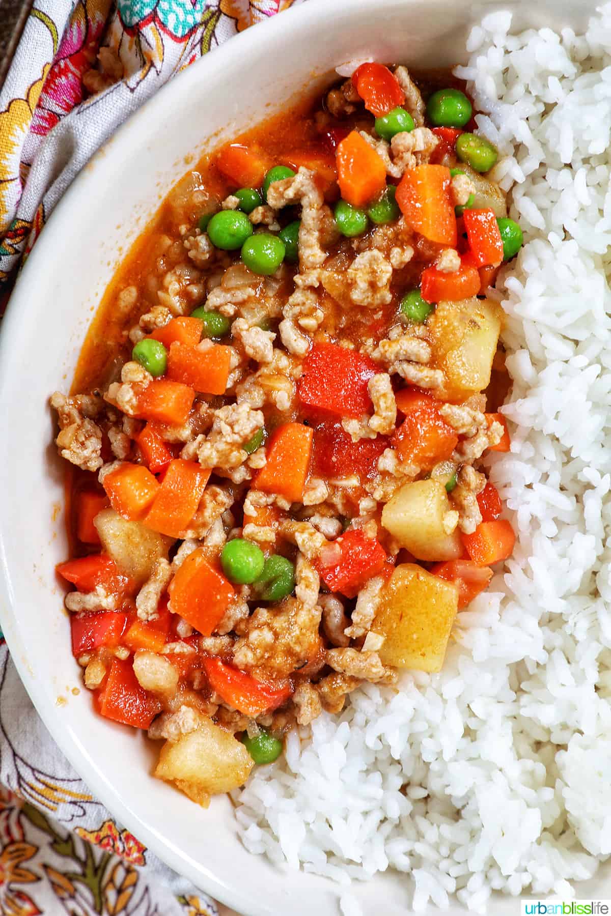 closeup of ground pork menudo over rice in a white bowl.