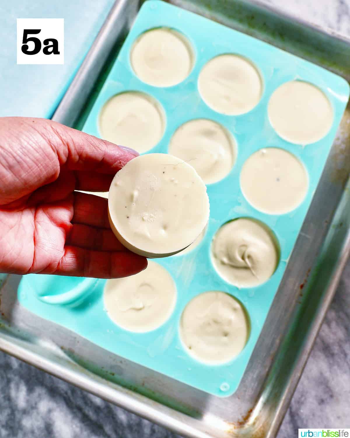 hand holding up a set white chocolate covered oreo cooke with filled blue candy mold in the background.