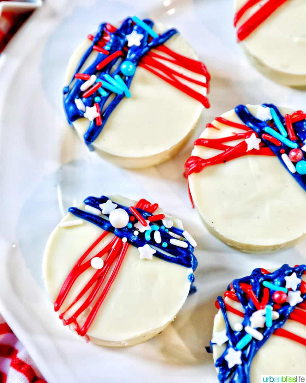 white plate with several white chocolate covered Oreo cookies with red and blue frosting and sprinkle decorations.