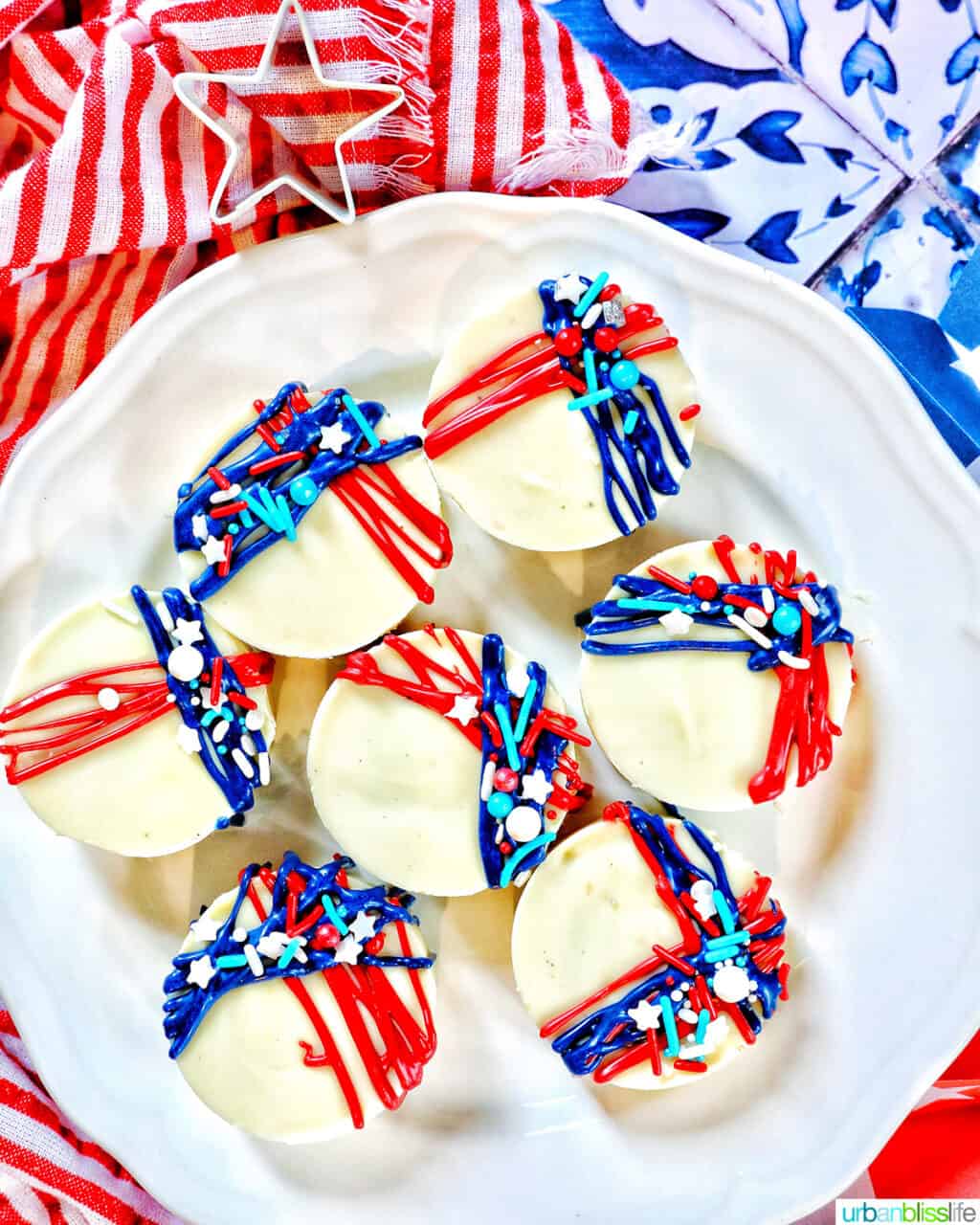 white plate with several white chocolate covered Oreo cookies with red and blue frosting and sprinkle decorations.