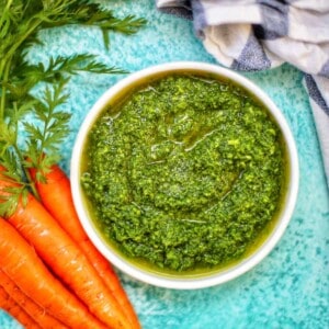 carrot top pesto in a bowl with carrots.