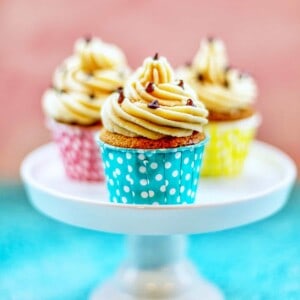 chocolate chip cupcakes with cookie dough frosting in blue, pink, and yellow cups on a pedestal.