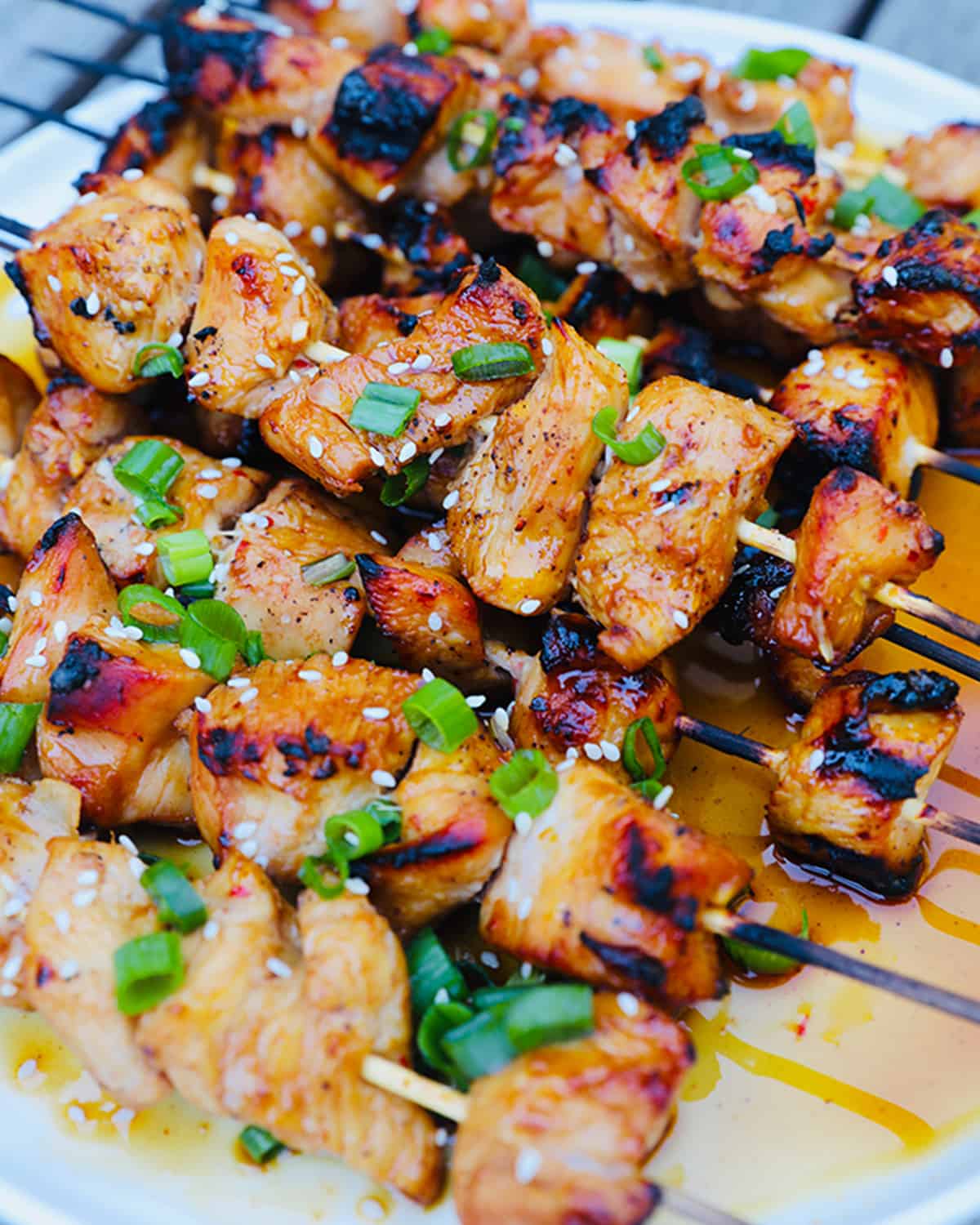 close up of honey garlic chicken skewers with green onion slices.