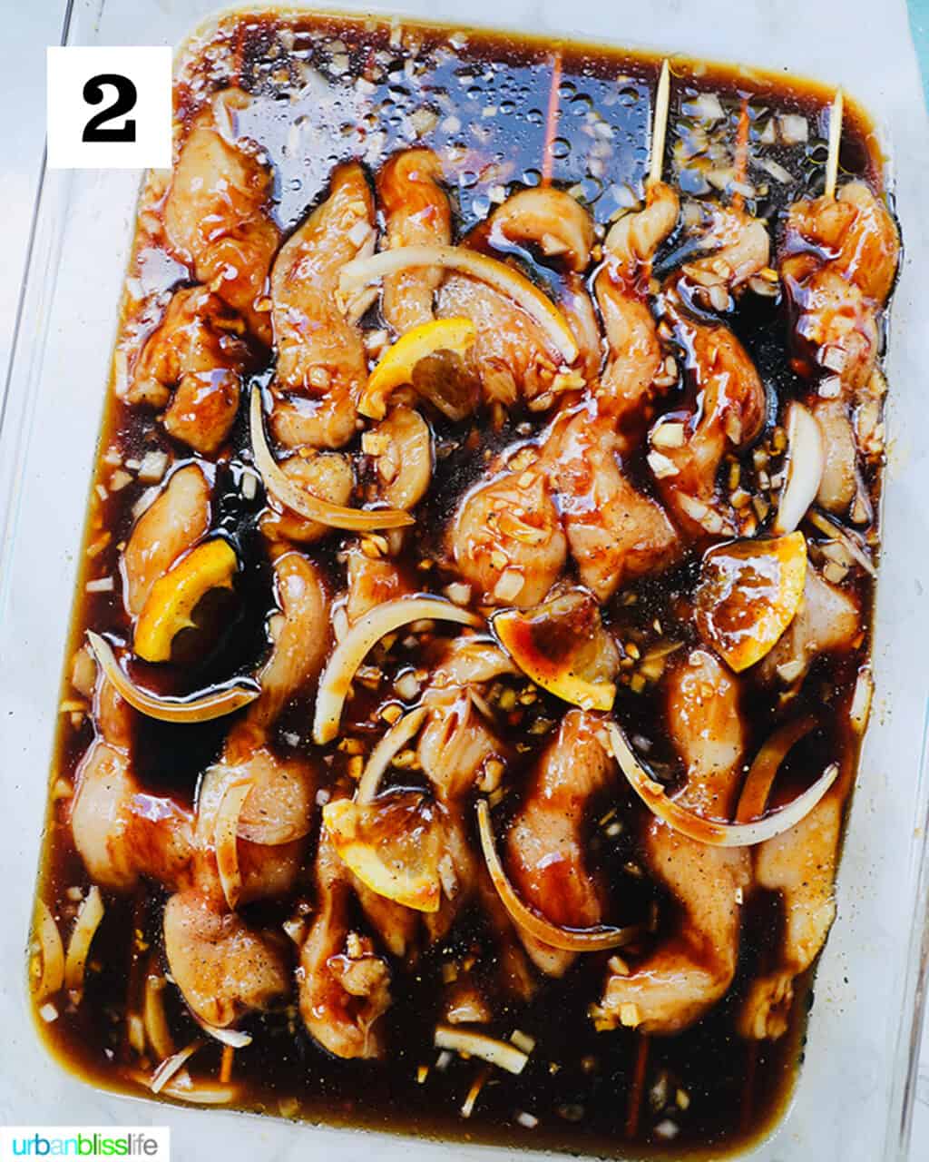 raw chicken skewers marinating in a large glass dish.