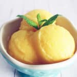 three balls of orange juice sorbet in a blue ice cream cup.
