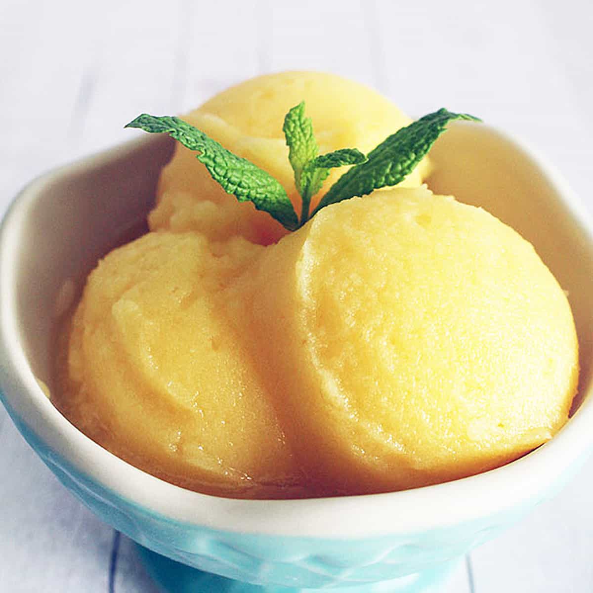 three balls of orange juice sorbet in a blue ice cream cup.