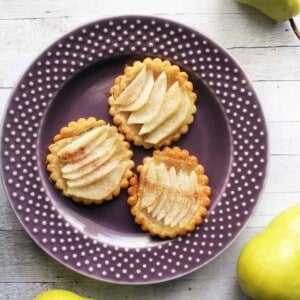 three baked pear tartlets on a purple plate.