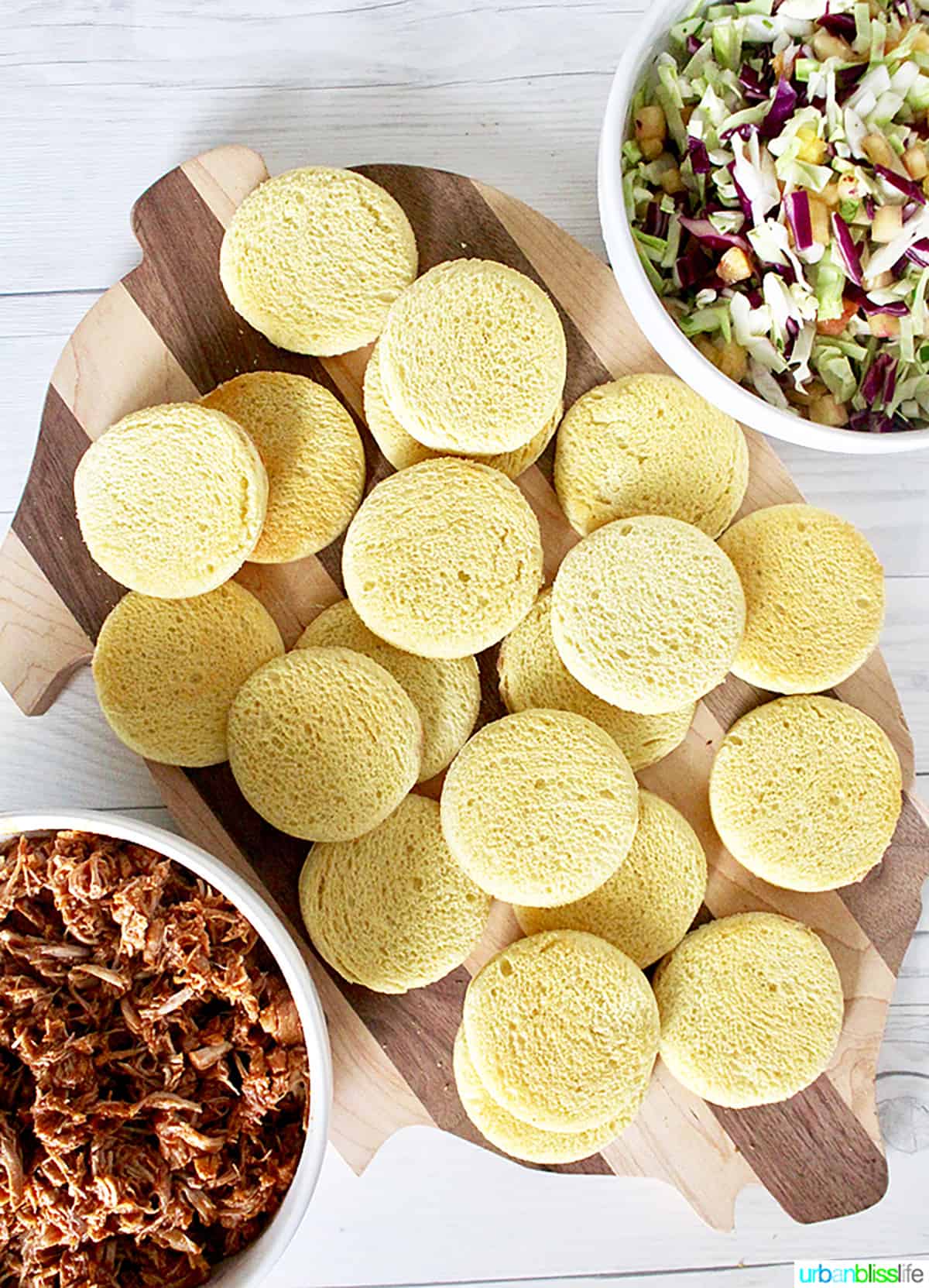 circles of hawaiian bread on a pig-shaped wooden cutting board and a bowl of pulled pork.