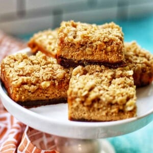 pumpkin cheesecake bars with gingersnap crust on a pedestal plate.