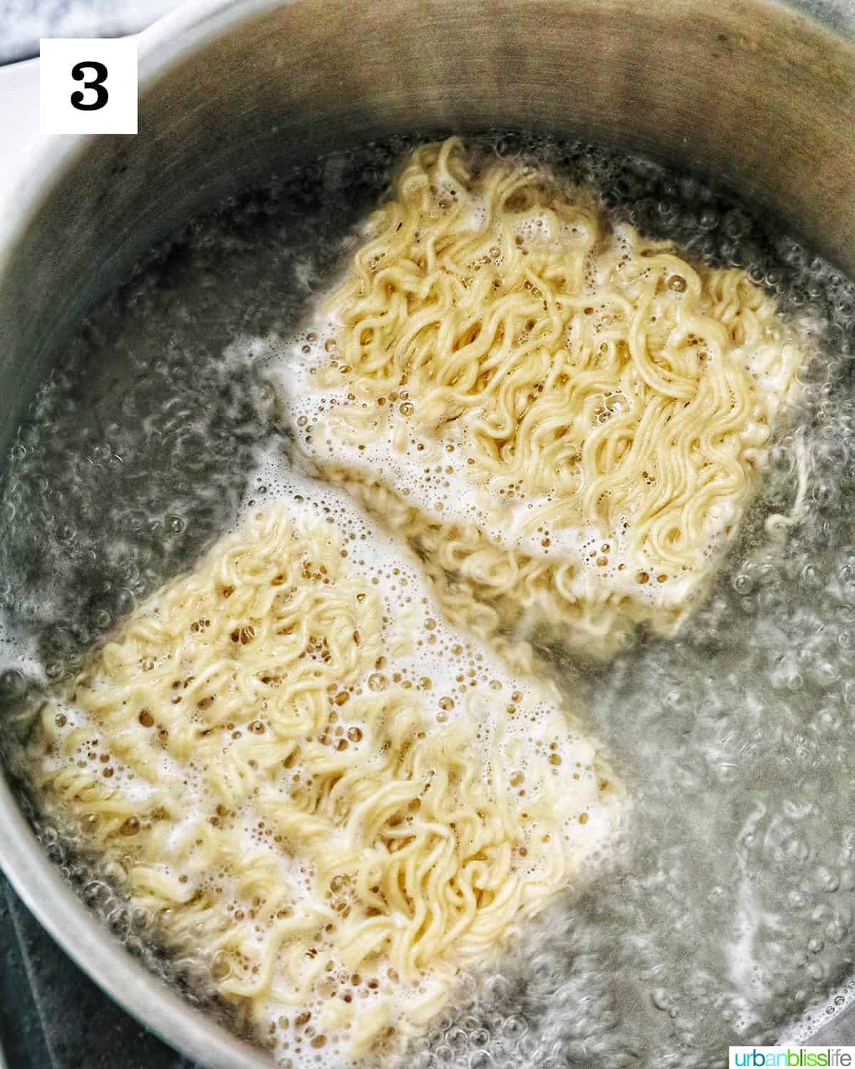 two packages of ramen noodles cooking in a large pot of boiling water.