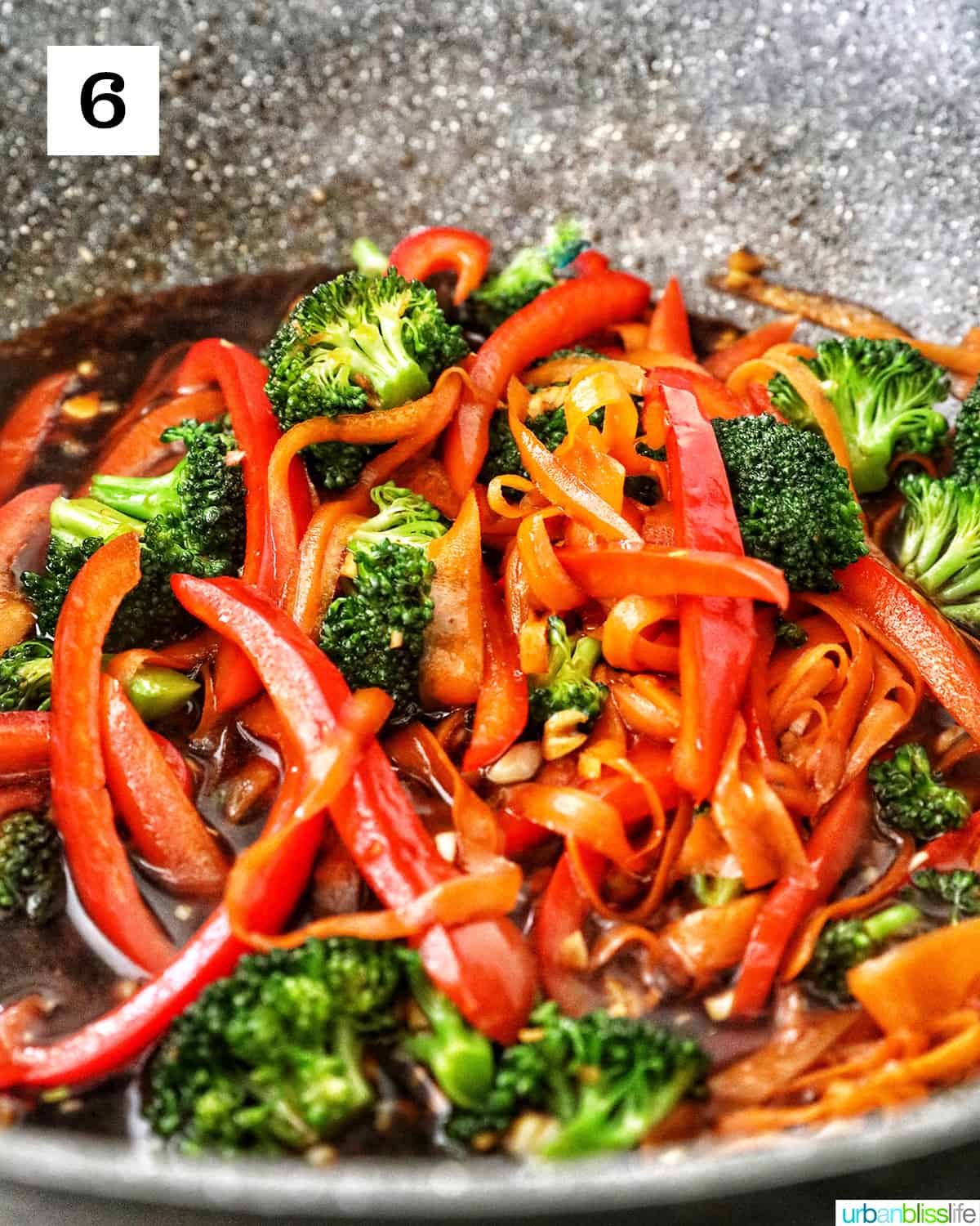 carrots, broccoli, red bell peppers stir-frying in a large wok with soy sauce.