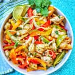 sheet pan chicken fajitas with peppers and a lime in a bowl.