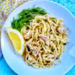 tuna pasta with capers and white wine sauce with a lemon wedge in a white bowl.