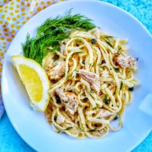 tuna pasta with capers and white wine sauce with a lemon wedge in a white bowl.
