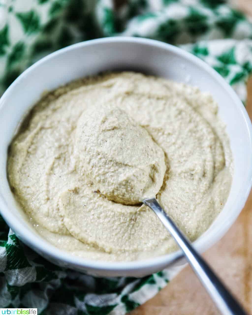 whitwhite bowl of Vegan Cashew Cheese with spoon in bowl, with green and white napkin underneath.