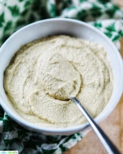 whitwhite bowl of Vegan Cashew Cheese with spoon in bowl, with green and white napkin underneath.