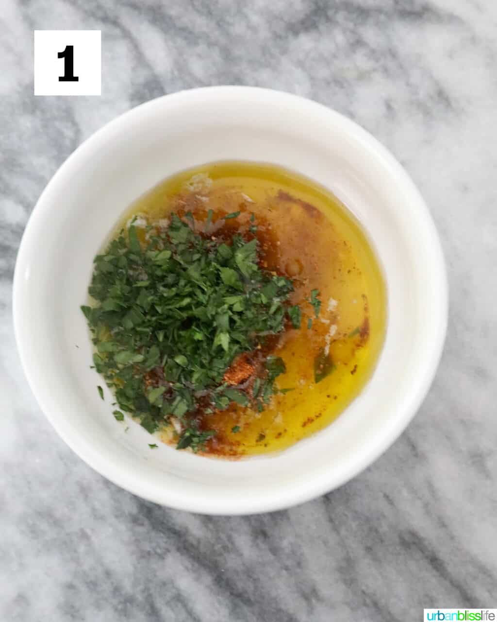 white bowl with butter, herbs, and seasonings on a marble table.