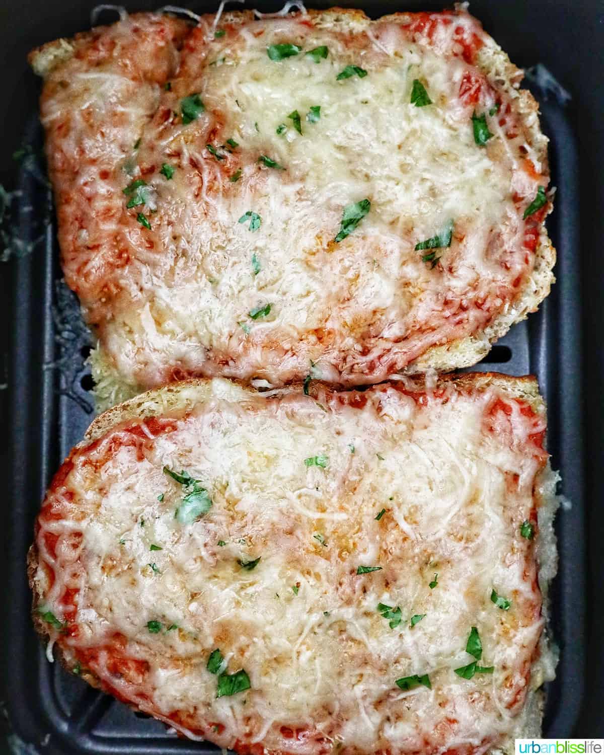 two half loaves of french bread pizza in an air fryer basket.