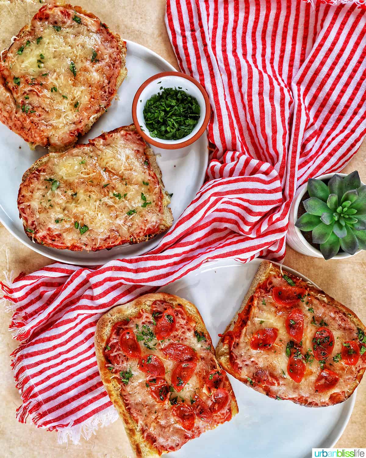 cheese french bread pizza and slices of pepperoni french bread pizza with a red striped napkin placed at angles on a marble table.