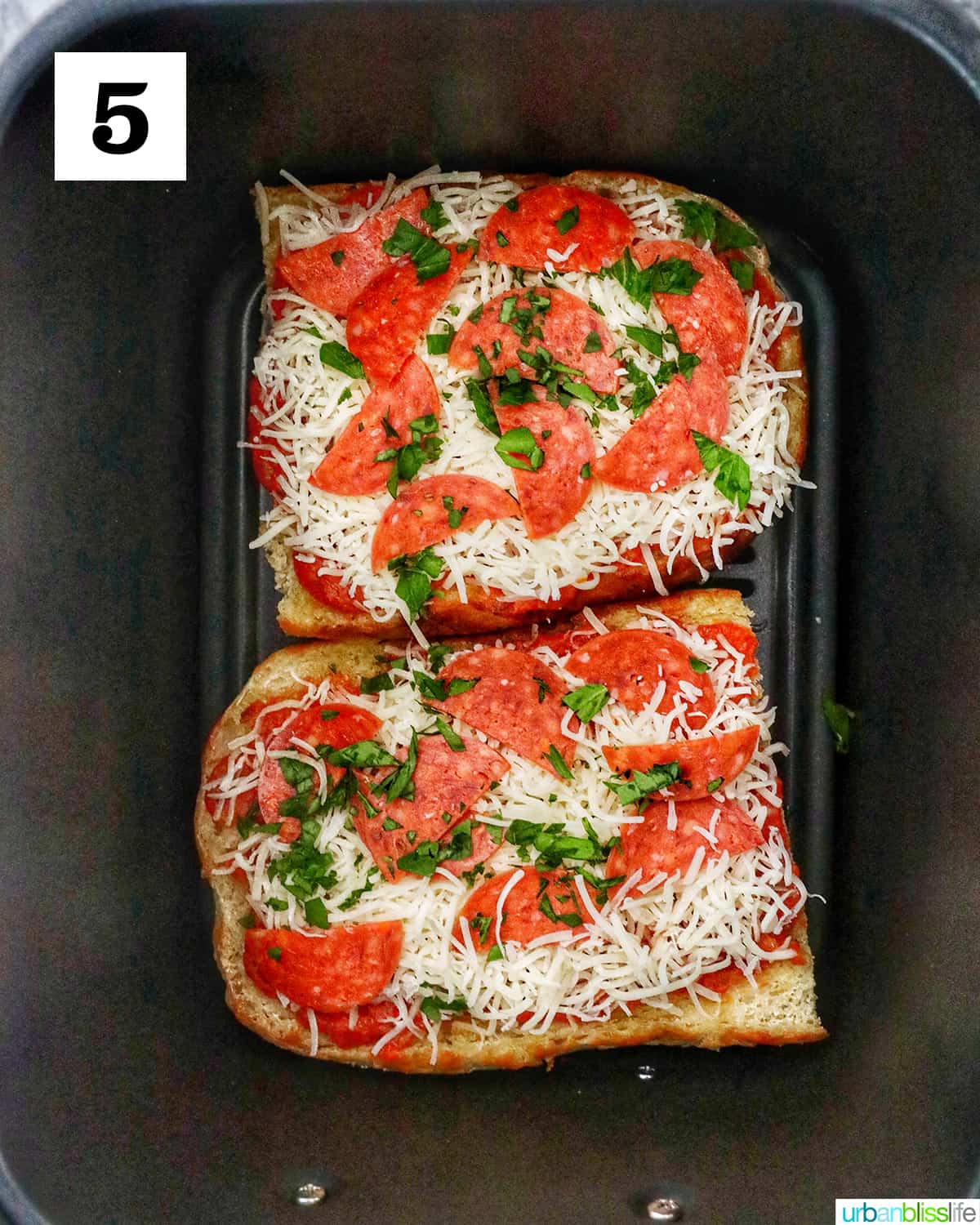 two french bread halves with pizza toppings in an air fryer basket.