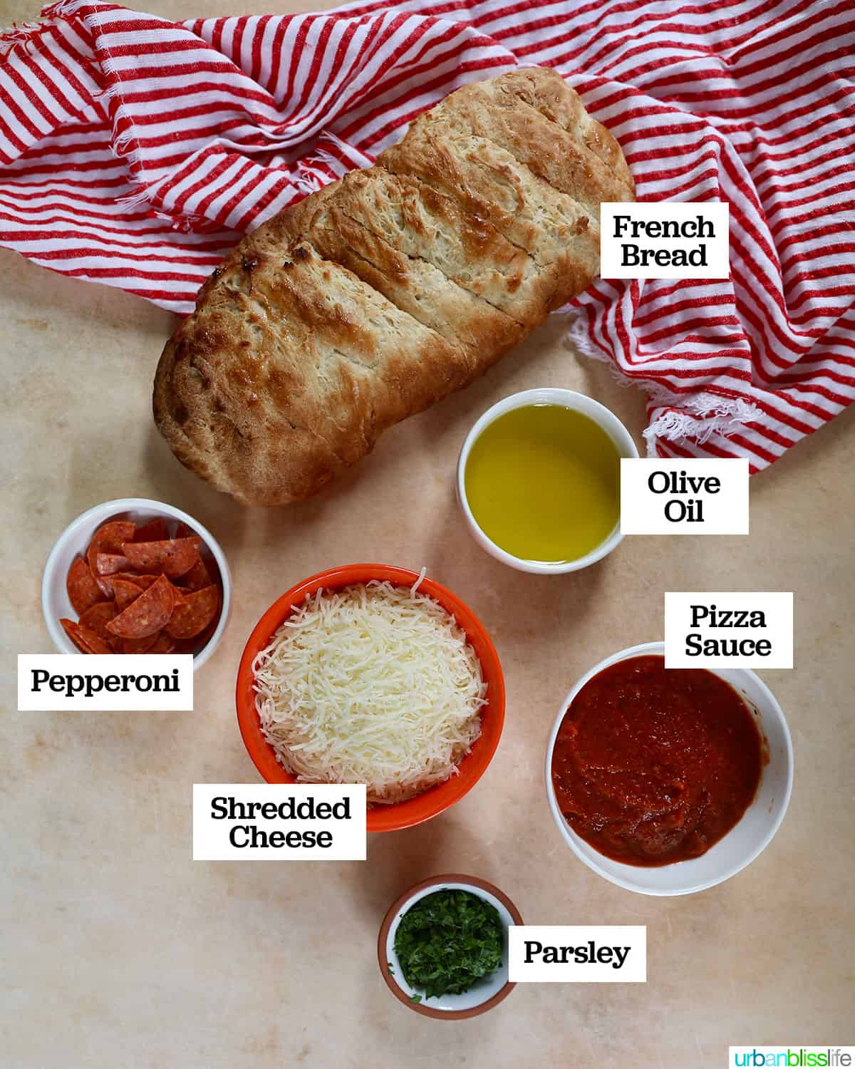 bowls of ingredients plus a loaf of french bread to make air fryer french bread pizza with red and white napkin.