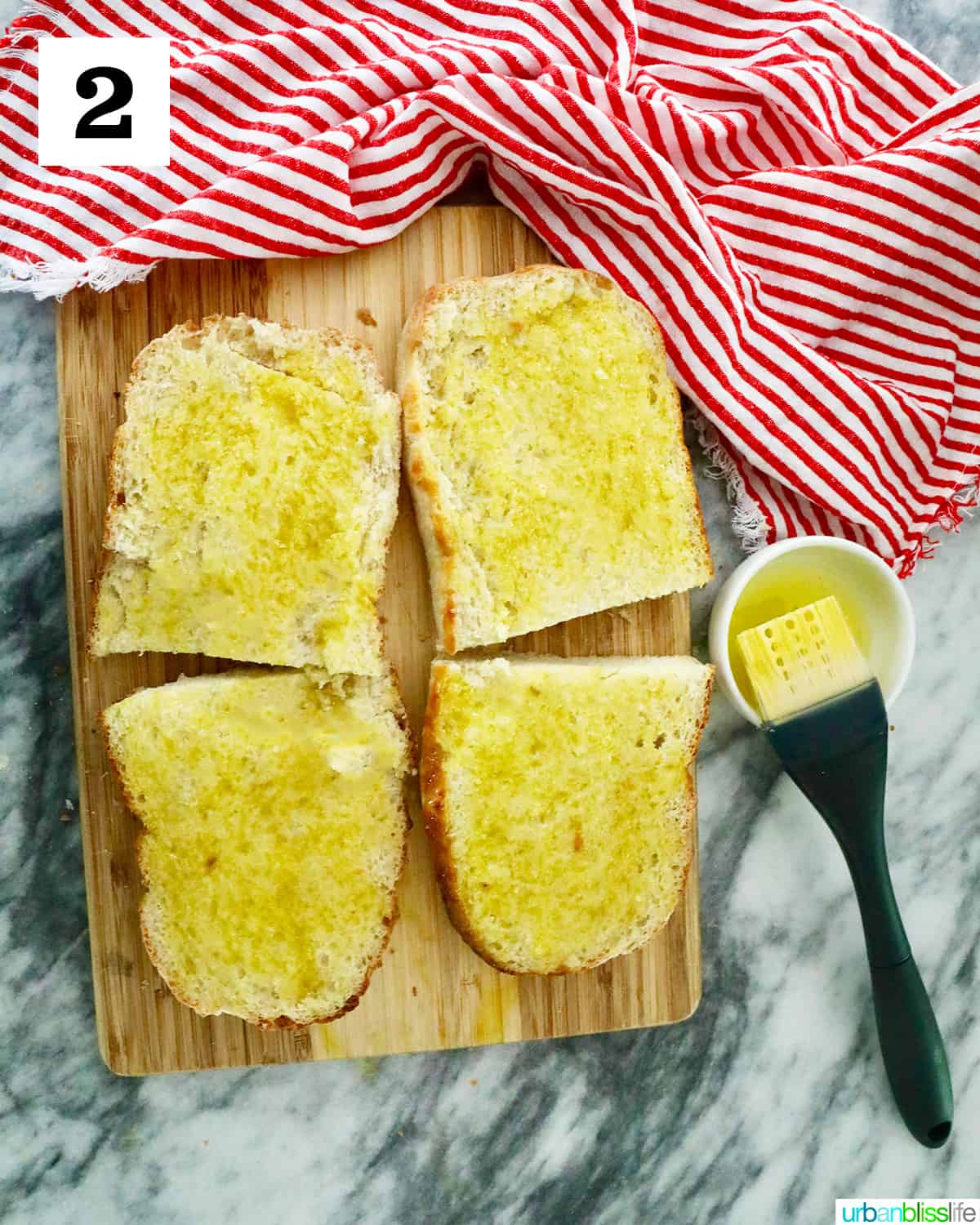 four sliced halves of french bread on a cutting board, topped with olive oil,  and red striped napkin with bread knife.