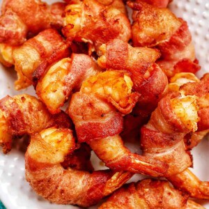 several bacon-wrapped shrimp stacked onto a white plate.