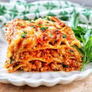 side view of multi-layered dairy free lasagna on a white plate with green and white napkin in background.