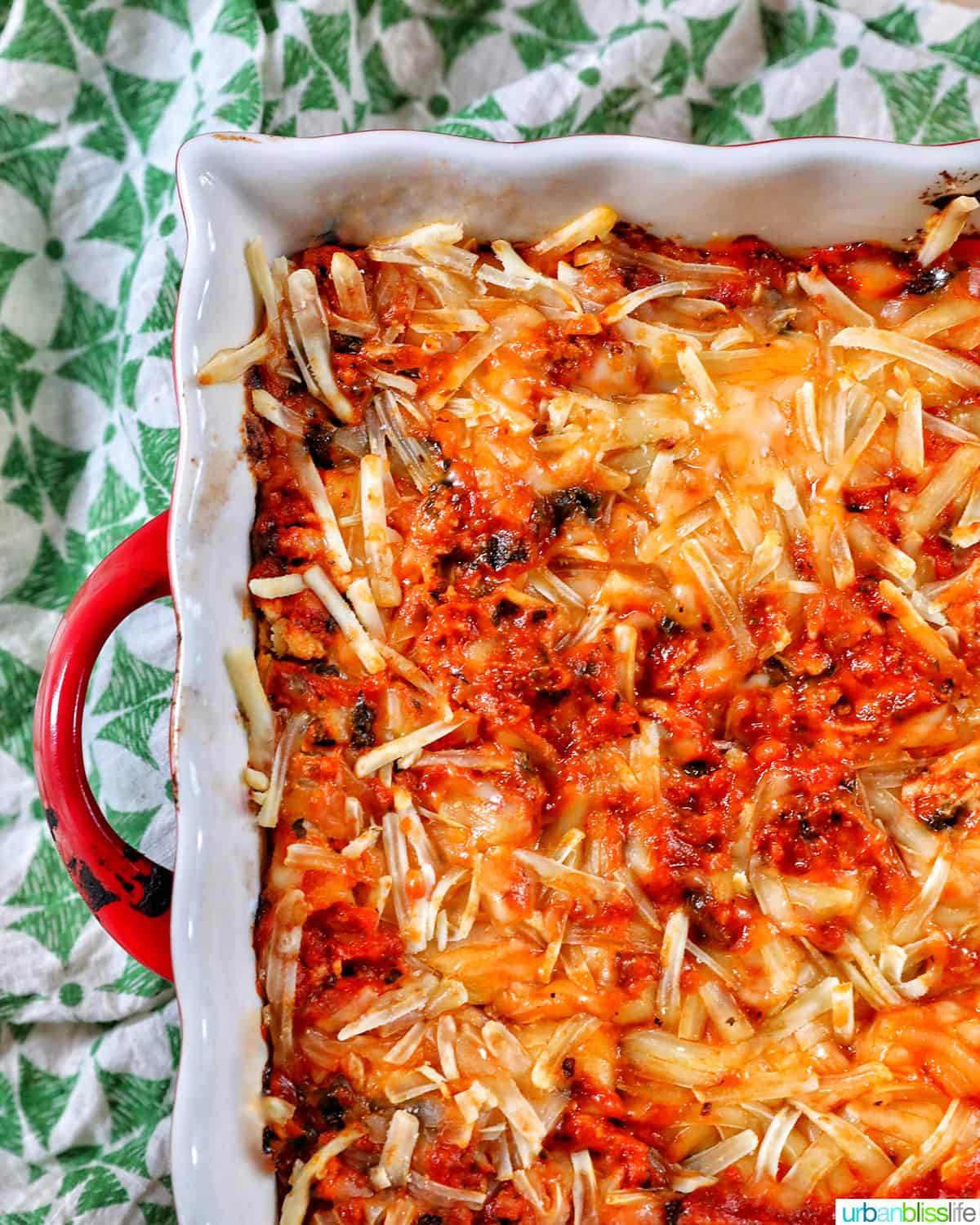 half side of a baking dish with red handle, filled with dairy free lasagna on a green and white napkin.