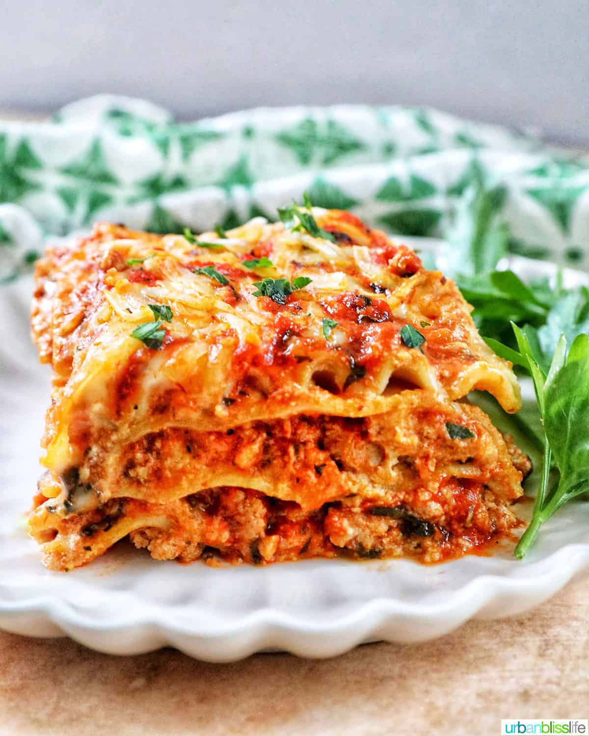 side view of multi-layered dairy free lasagna on a white plate with green and white napkin in background.